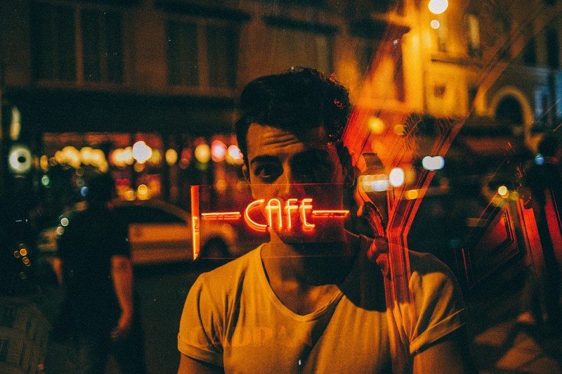 a man standing with a neon cafe sign covering his face in the window reflection, coffeebreak 4k