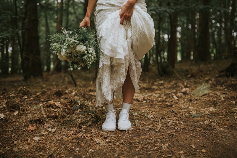 bride in white tennis shoes holds up her wedding dress train and bouquet in the woods, bride in the woods 4k