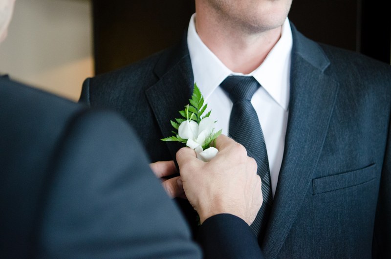 a groomsman in a suit pins a boutonniere on the groom who wears a black tie, a groom with boutonniere 4k