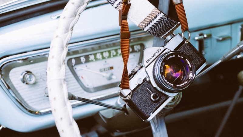 olympus camera and strap on top of a white steering wheel in a vintage car, classic in a classic 4k