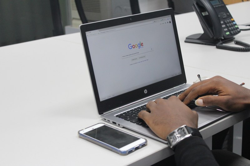 person with watch using laptop computer and google search engine with iphone on table, black entrepreneur 4k