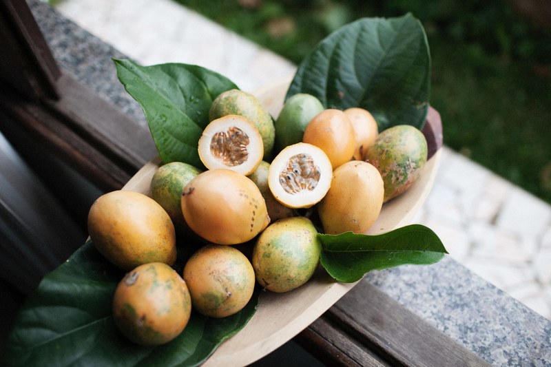 tropical orange and green fruit and leaves in a wooden bowl on a windowsill, tropical fruit bowl window 4k