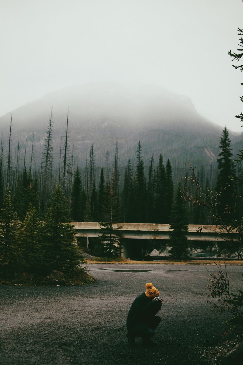 a crouching woman taking a photo on a stretch on asphalt with a misty hill on the horizon, crouching photographer 4k