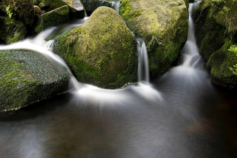 multiple waterfall streams flowing through mossy boulders, moss boulders and water streams 4k