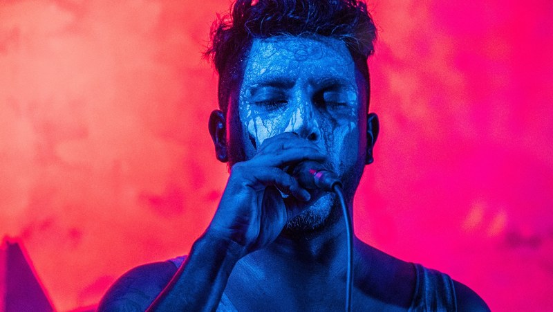 a man with a painted face singing into a microphone while illuminated with blue light, abduction plan 4k