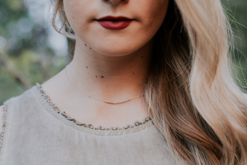 a close up of a womans chin she wears a necklace and dark red lipstick, _the simple truth 4k