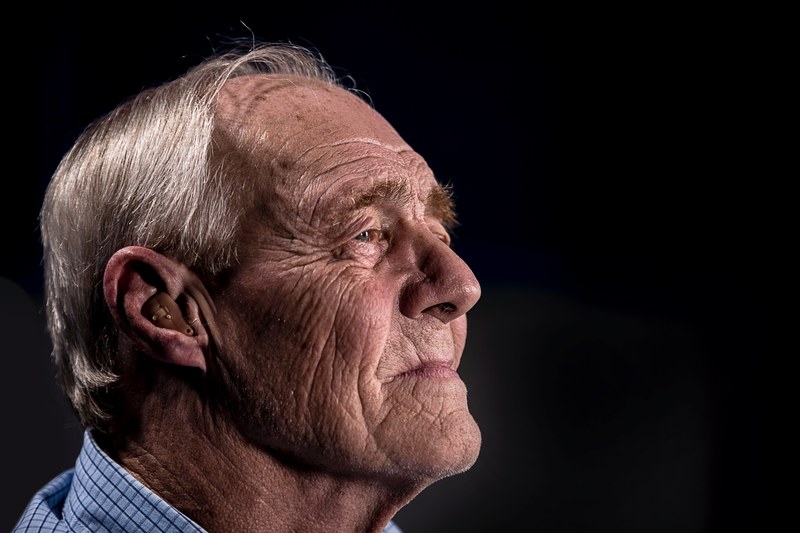 old man with wrinkle face and gray hair looking out and using a hearing aid, old man with hearing aid_ 4k