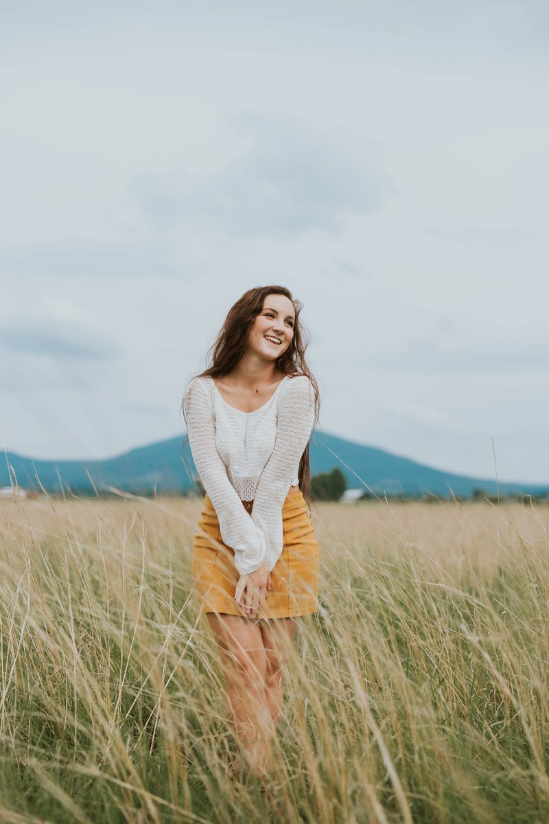 a woman wearing a skirt and long sleeve shirt standing in a field laughing, woman in a field 4k
