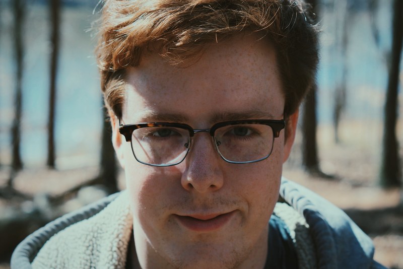a close up of a freckled man wearing glasses against a blurry outdoor background, close up man wearing glasses 4k