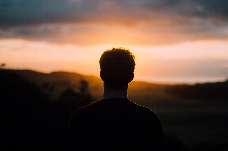 silhouette of the back of a mans head looking at the sun in a cloudy orange sky, man watching muriwai sunset 4k