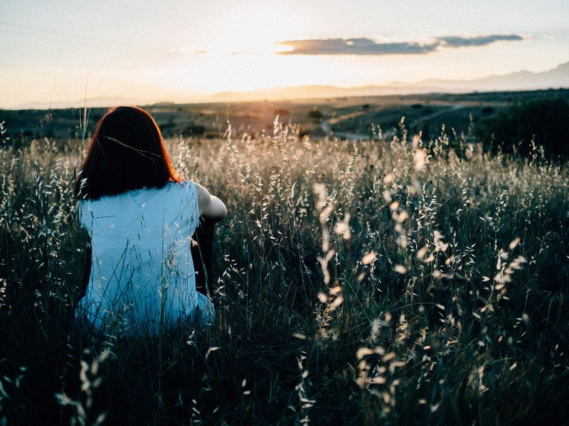 a girl sitting in a field in the countryside watching the sunset, sunset field views 4k