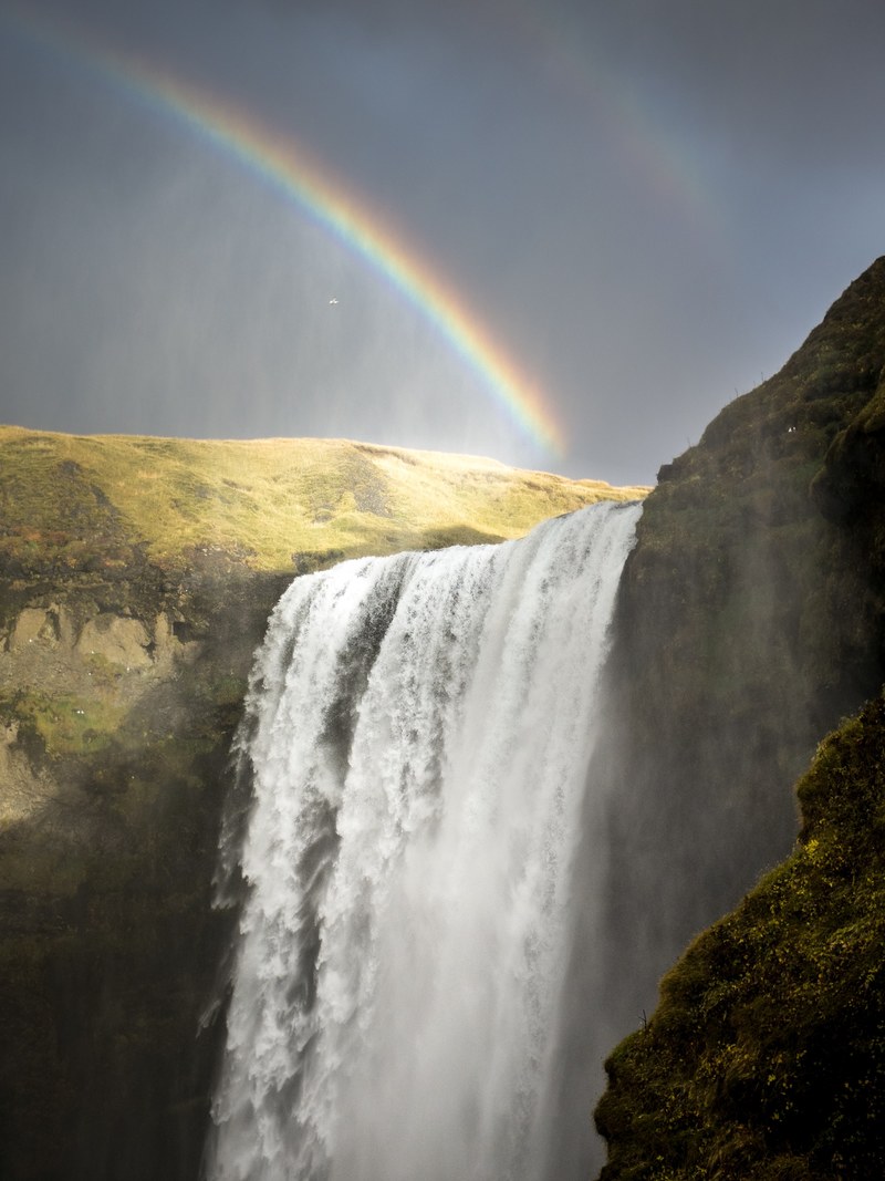 a rainbow over a waterfall pouring down from mossy rocks in skgafoss, rainbow over a waterfall 4k