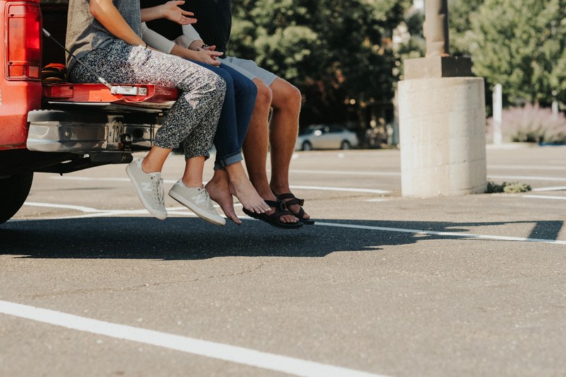 three people sitting on the tailgate of a red truck in a parking lot in fort collins, parking lot party 4k