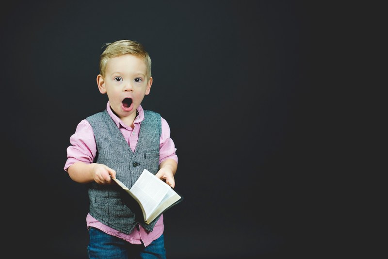 a little boy holding a book with a surprised expression on his face, the wonder of a book 4k