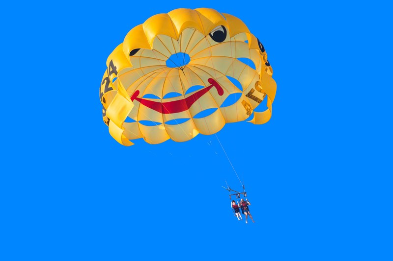 people parachuting across a blue sky with a yellow smiley face parachute, volando 4k