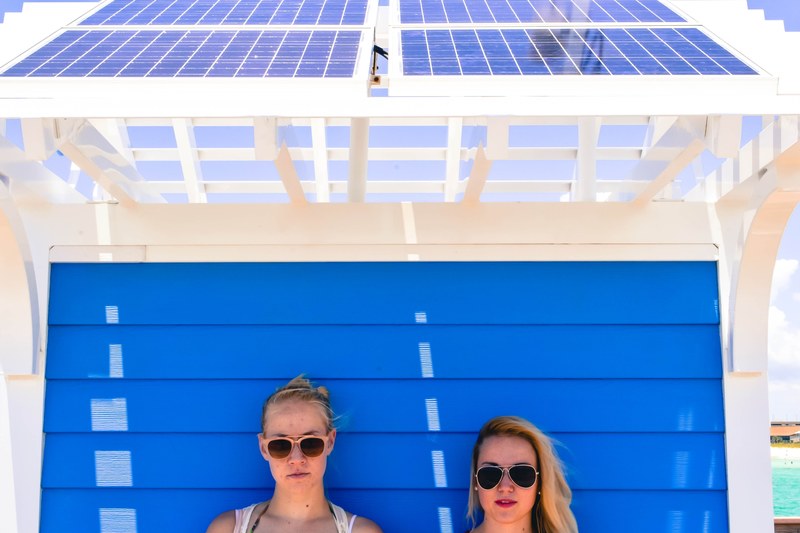 two young women posing in front of blue wooden wall beneath solar cells at panama city beach, two young women posing 4k