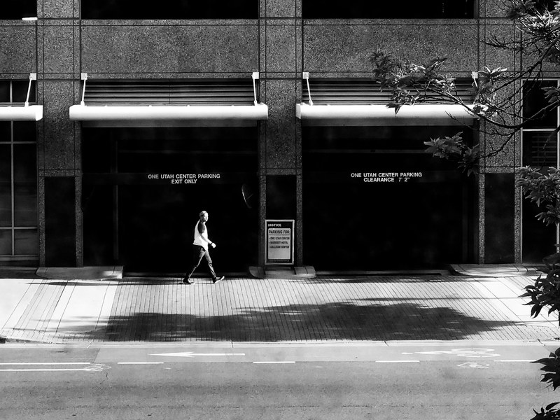 a black and white shot of a man walking past garage doors, city stroll 4k