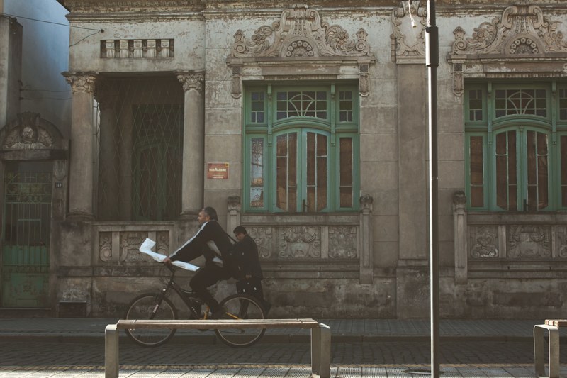 a man biking down the side of the road in a historic city, cyclist going down road 4k