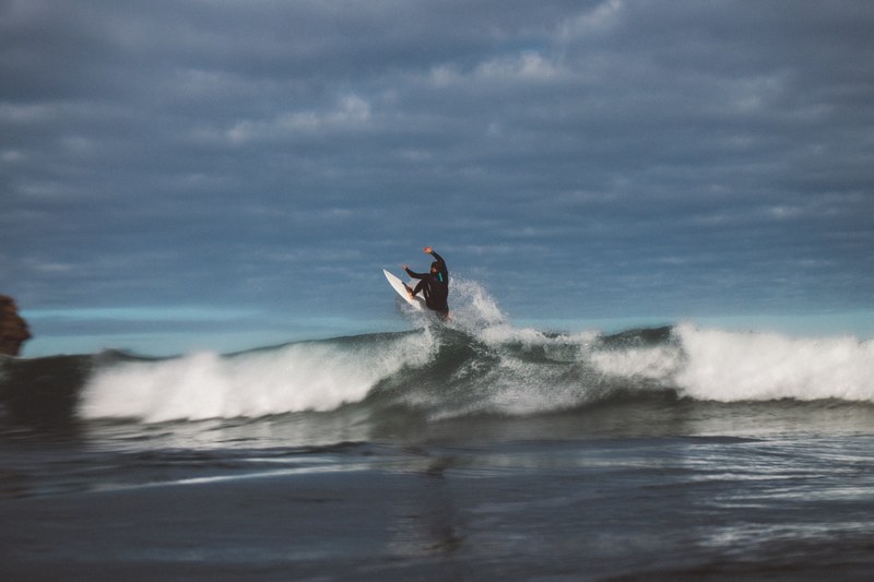a man riding a wave with a surfboard in piha new zealand, piha surf boarder 4k