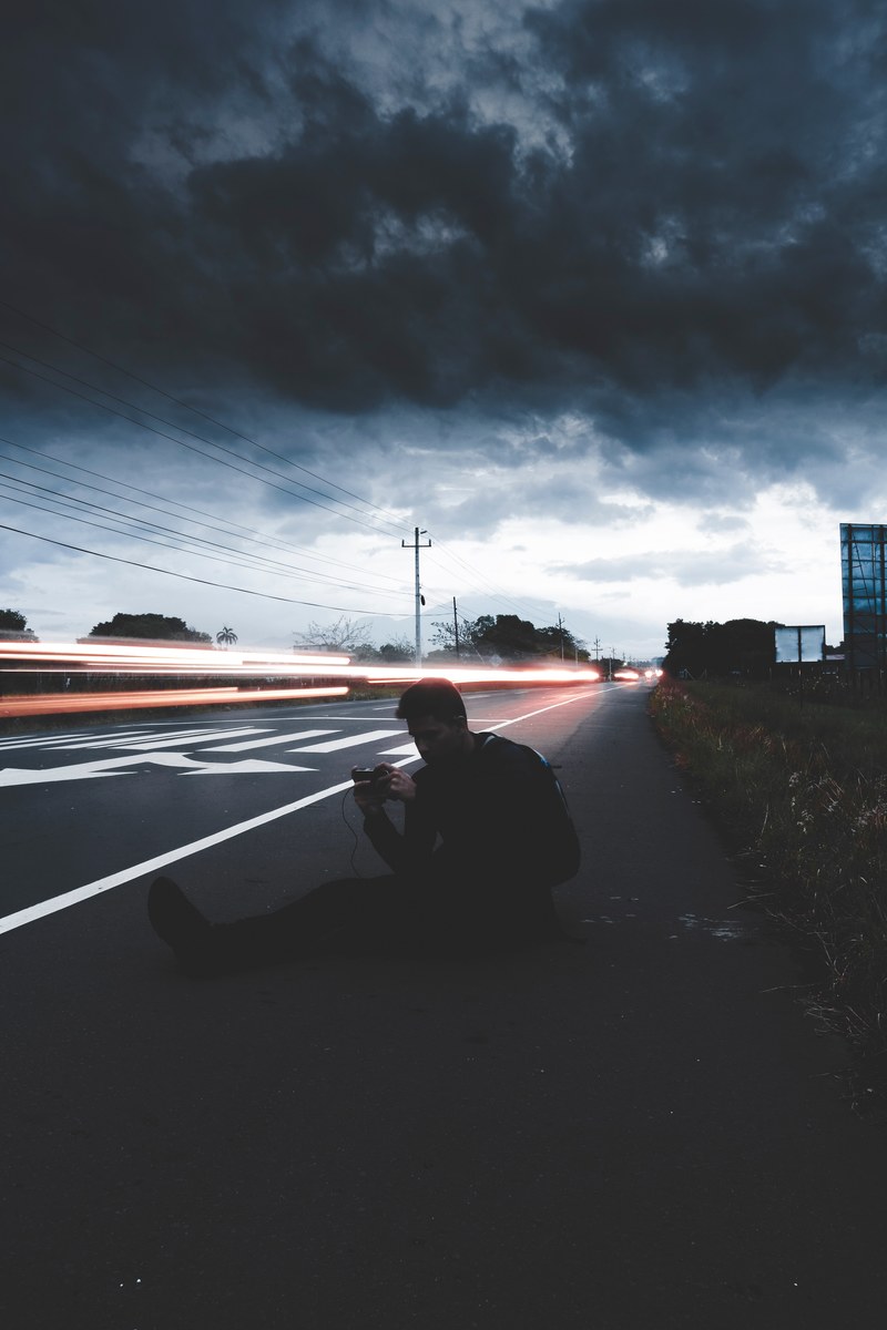 light trails on a road with a man seated on the roadside and using his phone, nrg 4k