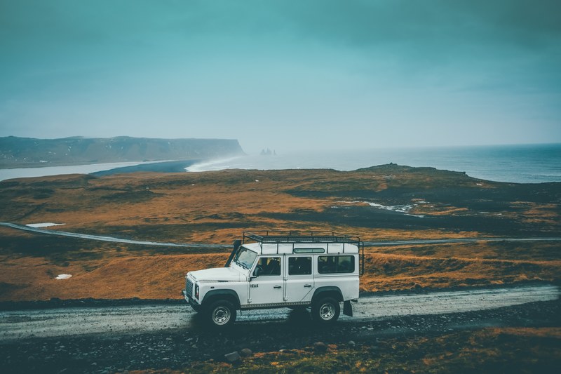 a white off road vehicle on a dirt road with a misty shoreline at the back, driving off road along the cold coast 4k