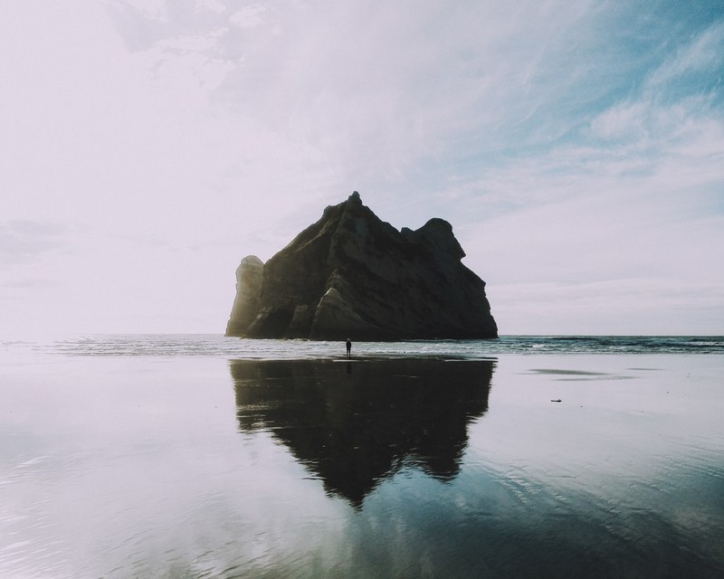 person standing in front of large rock island reflected in the water, large rock reflected in water 4k