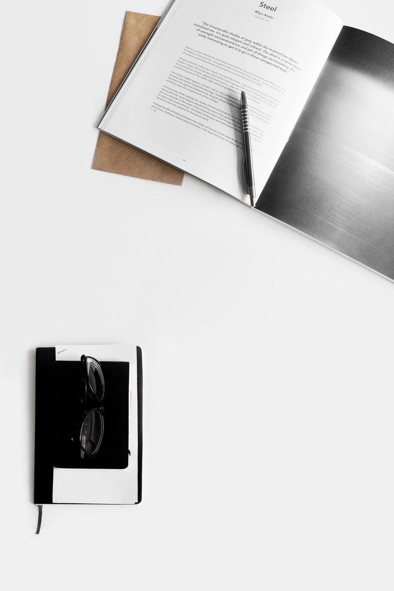 an overhead shot of a book a notebook and a pair of sunglasses on a white surface, flatlay 4k