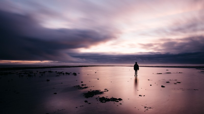 a lone man standing on a beach looking into a cloudy evening sky in grignon, contemplation_ 4k