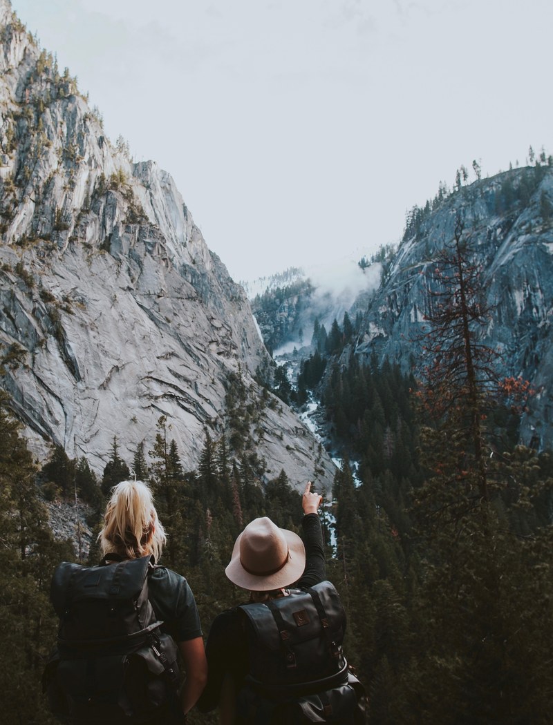 two women with large backpacks in a mountain pass in yosemite, waterfall in the distance 4k