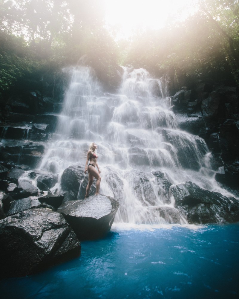 a woman in bikini on a wet rock near a waterfall, exploring bali 4k