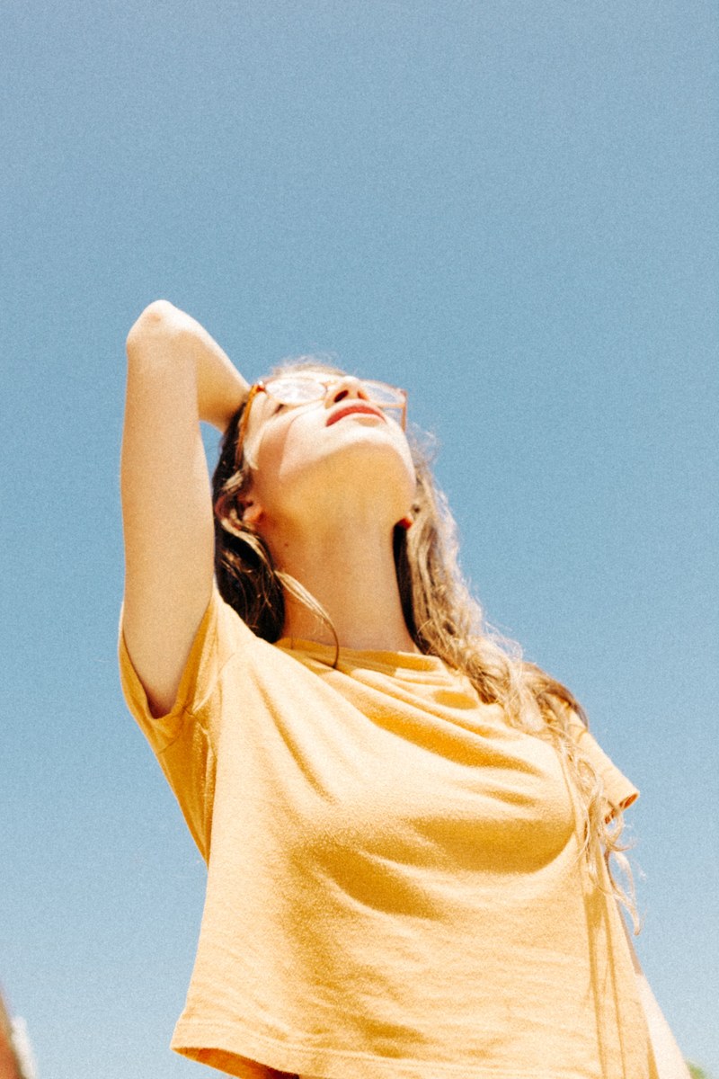 young woman in a yellow shirt and vintage glasses staring up at the sky, forever never 4k