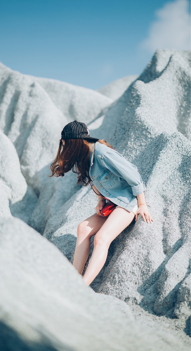 a woman in a baseball cap and denim shirt leans against sand dunes in thailand, woman leaning on sand dunes 4k