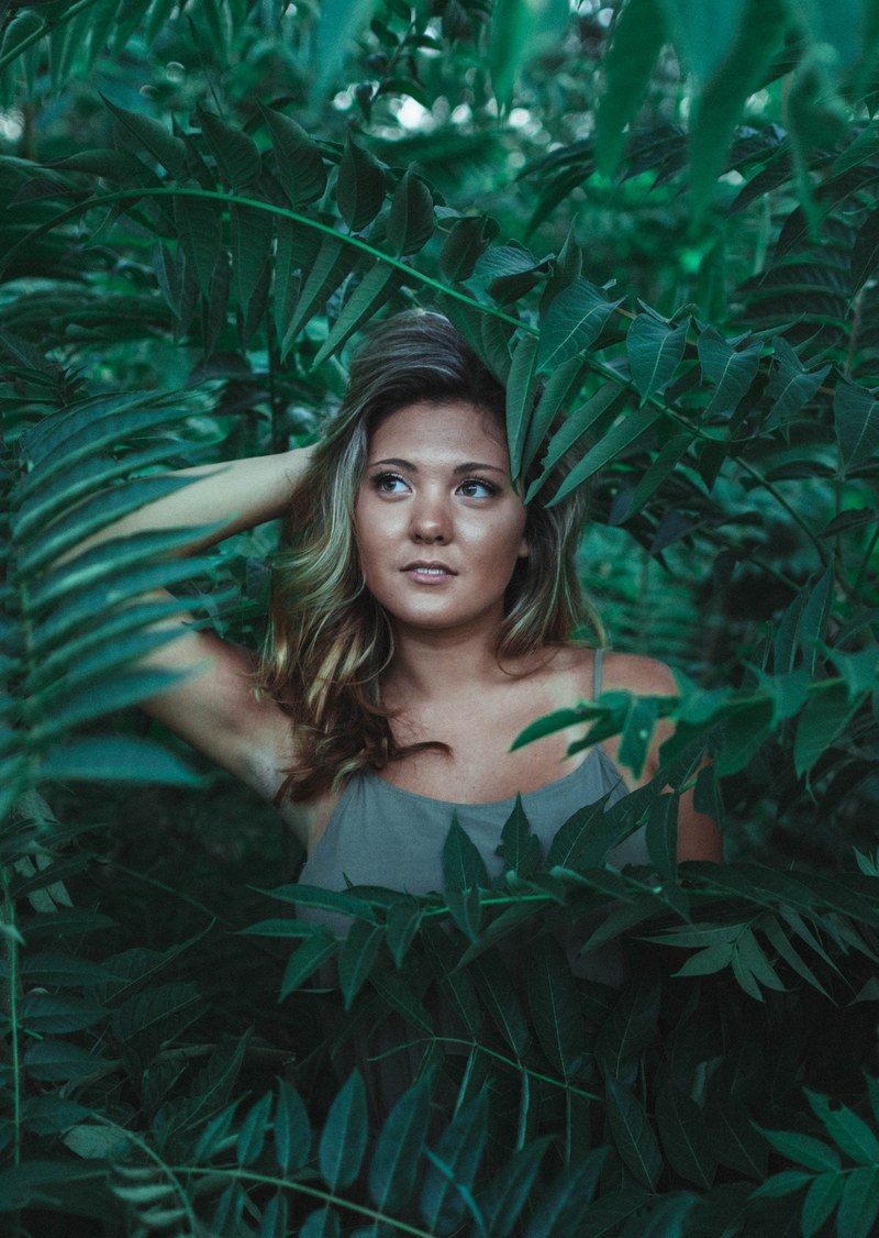 a model poses looking to the side among bright green ferns, in the brush 4k