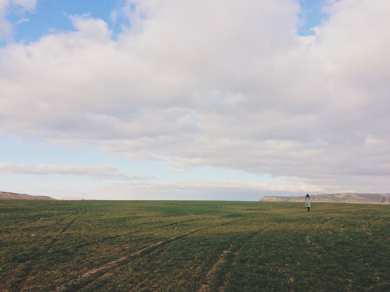 woman stands alone in a green farm field and a cloudy blue day, alone in the field 4k