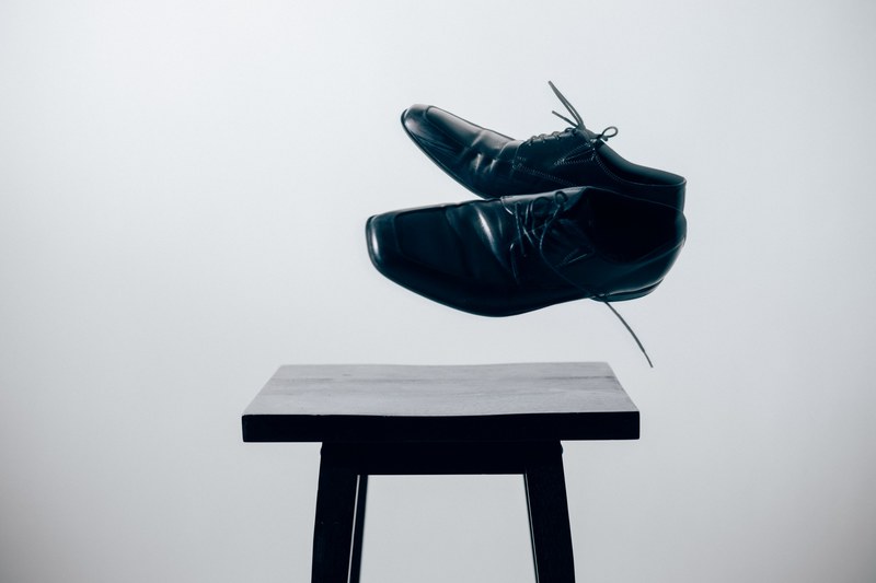 two black leather shoes suspended over a black stool, leather shoes over a stool 4k