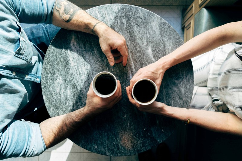 two people holding cups of coffee while seated opposite to each other at a round table, coffee talks 4k