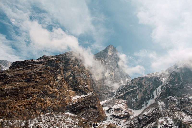 a high mountain top towering over two other peaks under a cloudy sky, three mountain peaks 4k