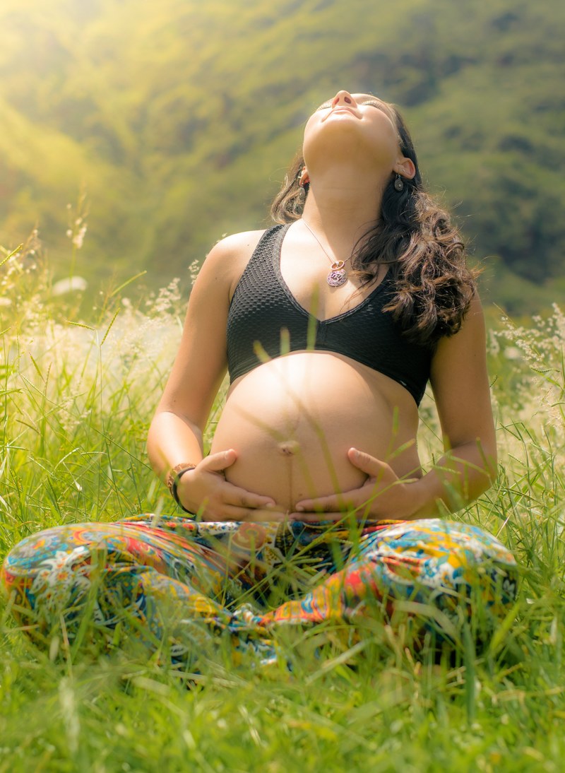 a dark haired pregnant woman with her stomach exposed sitting cross legged on the grass, expecting mother on the grass 4k