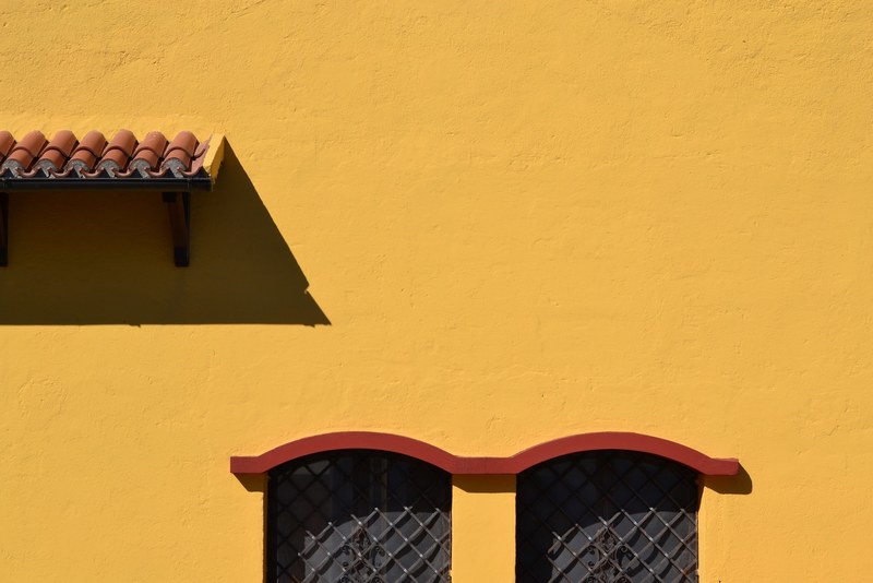 a tiled awning windows with grills and curved molding on an ochre colored wall in sirolo, _lost in yellow 4k