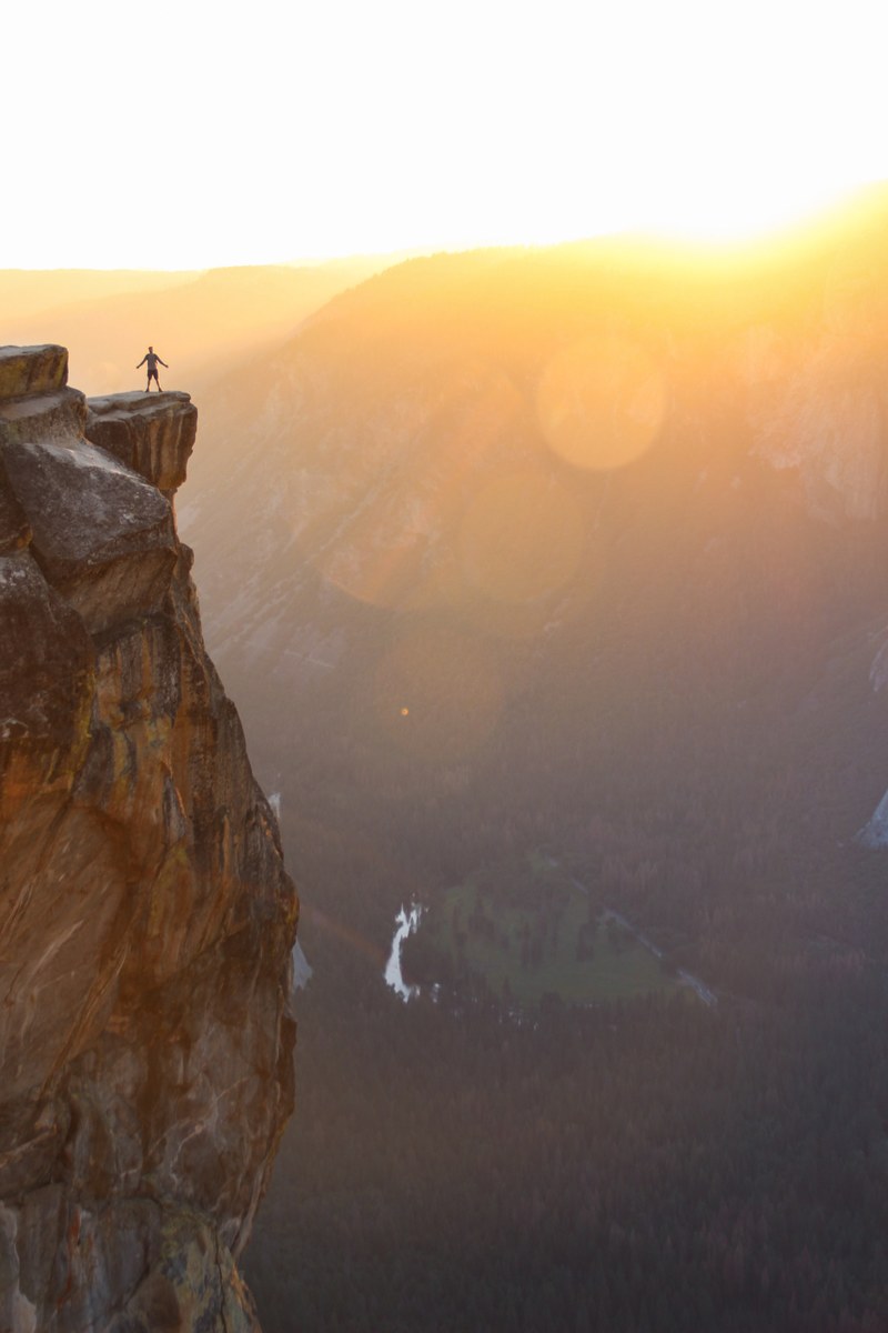 person with arms stretched wide standing by the ledge of a cliff during sunrise in yosemite valley, on top of the world 4k