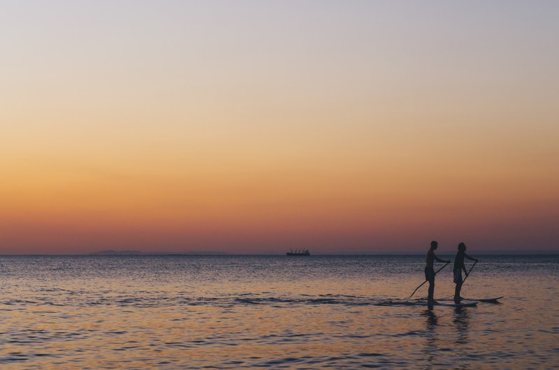 two silhouettes paddleboarding through the calm ocean of brighton beach during a dull sunset, sunset paddleboarding in brighton 4k