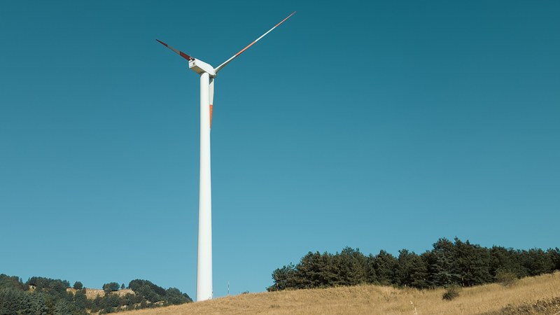 lone wind turbine on a grassy hilltop on a bright blue day, windmill on a hill 4k