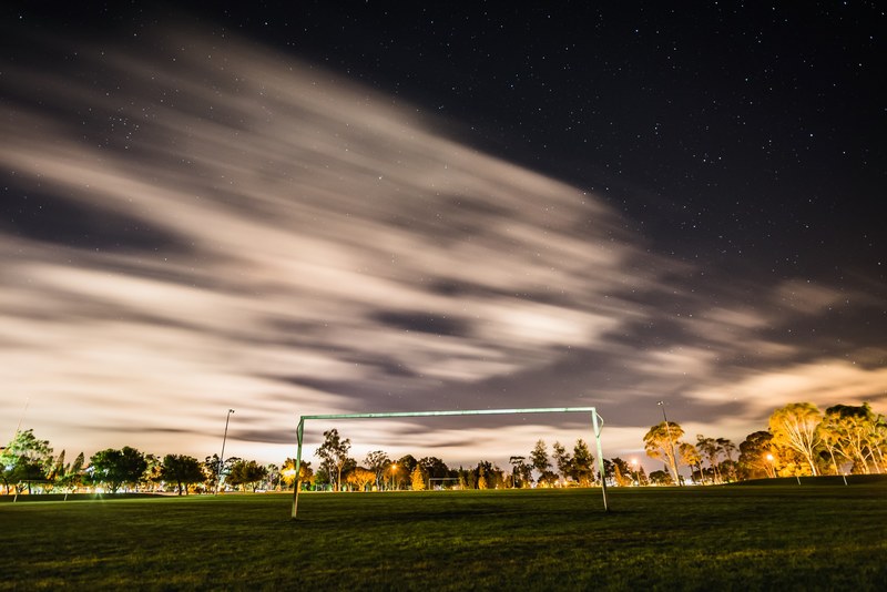a soccer field at night with stars blurred in the sky, soccer goal construction with night sky clouds 4k