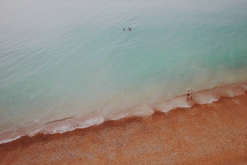 drone view of people swimming in clear ocean washing up on red sand beach in brighton, drone view of red sand beach 4k