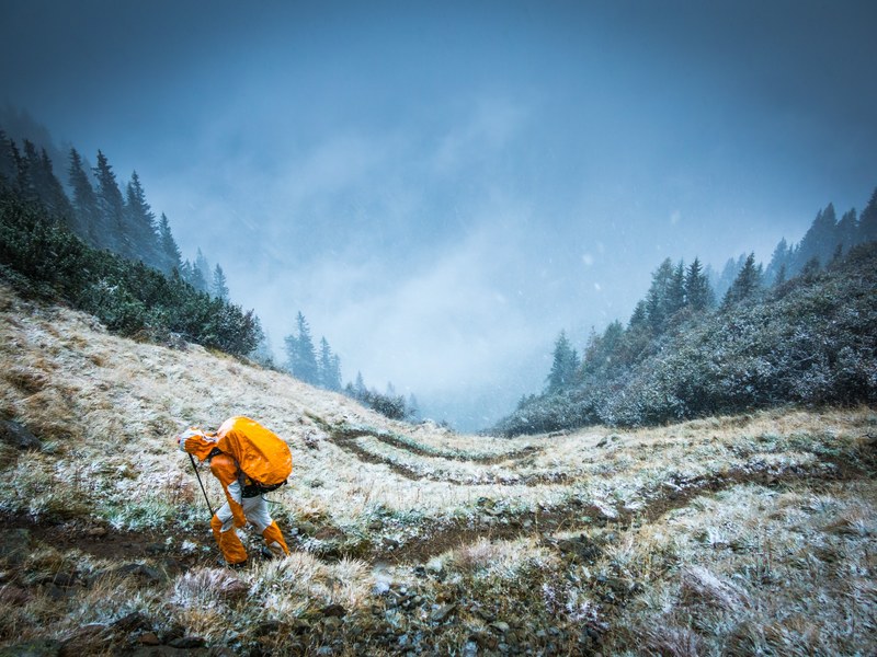 a mountaineer in bright orange clothes on a grassy slope in winter, mountaineer on a slope 4k
