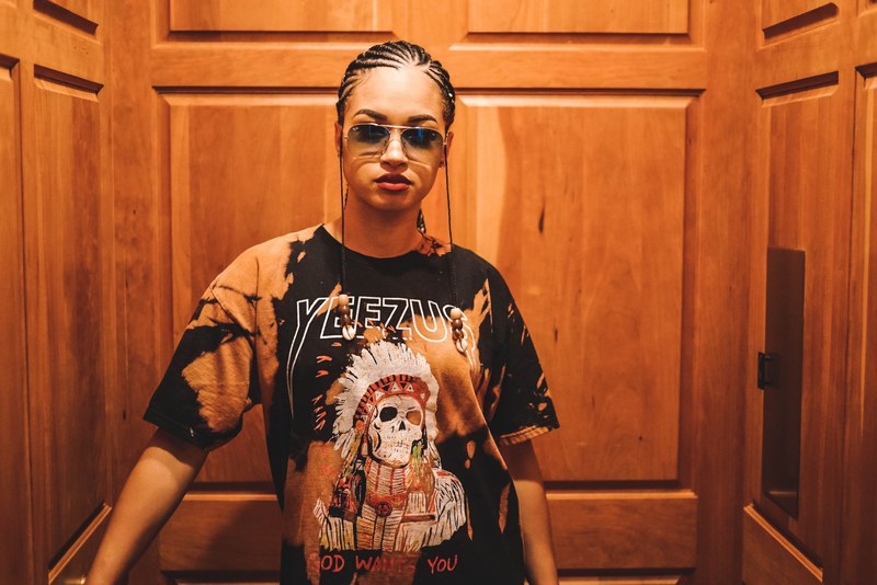 trendy woman with cornrow braids and a yeezus t shirt in an elevator, lost in the glasses 4k