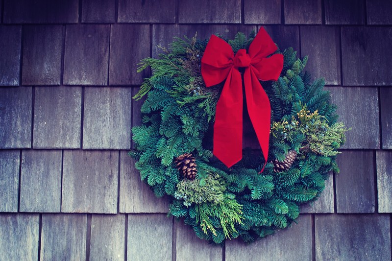 a christmas wreath with a red bow and pinecones hanging on the side of a shingled house, wreath 4k