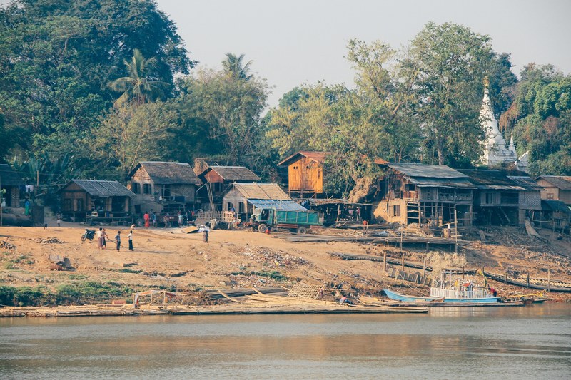 a small village with wooden houses trees few people and a river next to it in old began, _to bagan in myanmar 4k