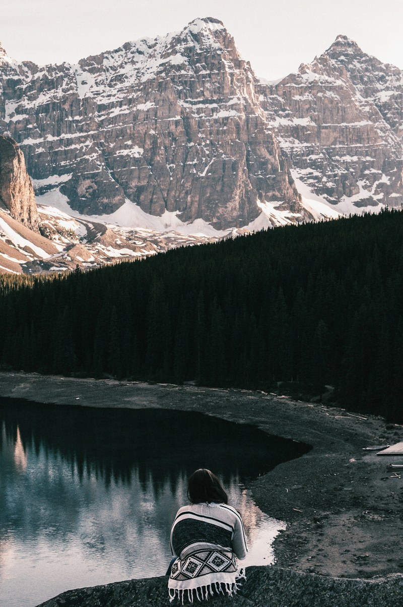 woman looks out over moraine lake snowy mountain and evergreen trees, woman looks out at moraine lake 4k