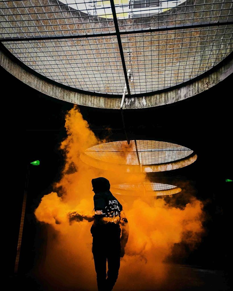 silhouette of person in a hood running through orange smoke underground, smoke time 4k